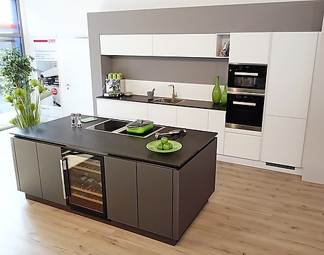 Kochinsel mit Muldenlüftung und Weinkühler. Hochschränke (auch getrennt von Spülzeile stellbar) mit Dampfgarer & Mikrowelle, Pyrolyse-Backofen mit Klimagaren und Kühlzentrum mit 0°-Zone. Schöne Details wie Eiche-Besteckeinsätze und Edelstahl-Armatur! - X2 GLASLINE MATT. Ihre neue Lieblingsküche: Luxus mit edlen Mattglasfronten in Kristallweiß & Lavaschwarz sowie aufwändig geflammtem & gebürstetem Naturstein. Perfektes Grifflosdesign mit farblich jeweils abgestimmter, um die Insel umlaufender Griffmulde!