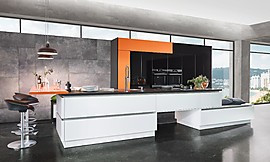 Diese Designerküche in Schwarz, Weiß und Orange zeigt sich geradlinig in ihrer teils grifflosen, teils mit Griffspuren ausgestatteten Ausführung. Niedrig geplante Schränke können zudem als Sitzmöglichkeit genutzt werden und sorgen für Wohncharakter. Zuordnung: Stil Design-Küchen, Planungsart Küche mit Sitzgelegenheit