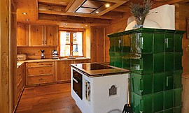 Inmitten der rustikalen Holzküche wurde eine Insel in Steinoptik mit Ofen eingeplant. Zuordnung: Stil Landhausküchen, Planungsart Küche mit Küchen-Insel