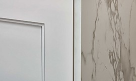 Hochglänzend weiß lackierte Kassettenfront umrahmt von einer weiß marmorierten Arbeitsplatte und Wange. Zuordnung: Stil Landhausküchen, Planungsart Detail Küchenplanung