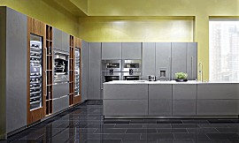 Die Designküche MILANO NUOVO vereint das kühle Grau von Edelstahl-Oberflächen mit warmen Akzenten in Olivenholz-Dekor. Zuordnung: Stil Design-Küchen, Planungsart Küchenzeile