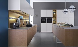Eine Küche in Weiß und Holz fügt sich in nahezu jede Wohnumgebung ein und kann als klassisch-modern bezeichnet werden. Bei dieser schönen Küche mit Kochinsel auf Kufen, &quot;schwebend&quot; an die Wand montierten Unterschränken, sowie Fronten aus Eiche und Lack, stimmen auch die inneren Werte: dezent in den Hängeschrank integriert befindet sich eine hochwertige Dunstabzugshaube, die ohne Abluftleitungen funktioniert. Zuordnung: Stil Design-Küchen, Planungsart Küche mit Sitzgelegenheit