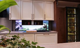 Weiße Holzküche mit Rahmenfronten und beleuchteter Küchenrückwand. Zuordnung: Stil Landhausküchen, Planungsart Küche mit Küchen-Insel