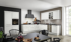 Beim Design der Küche handelt es sich um eine skandinavische Interpretation der Landhausküche. Die matten Fronten in Weiß wirken kühl und lassen zudem den Raum groß wirken. Die dunkle Arbeitsplatte und die Dunstabzugshaube setzen hier einen schönen Kontrast. Zuordnung: Stil Landhausküchen, Planungsart Offene Küche (Wohnküche)