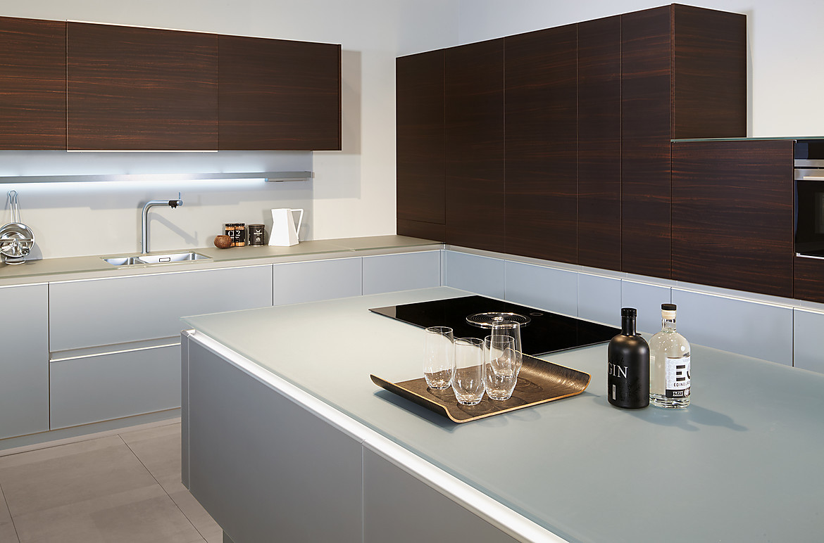 Designküche mit edel anmutender Glas-Arbeitsplatte in einem hellen und zeitlosen Grauton. Zuordnung: Stil Design-Küchen, Planungsart Detail Küchenplanung
