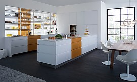 Leicht und lichtdurchflutet wirkt die designorientierte weiße Küche mit Retro-Elementen, die hier zu sehen ist. Die Linienführung in der zweizeiligen Küche betont klar und deutlich die Vertikale; die durchgehend grifflosen Fronten bei beiden Küchenzeilen und der Gerätehochschrank-Wand verschreiben sich dem minimalistischen Designküchen-Gedanken. Den Reiz macht der sparsame und feinfühlige Einsatz der Retro-Designfarbe „curcuma“ aus. Irgendwo zwischen Orange und Senfgelb setzt diese Trendfarbe einen frischen Akzent in der ansonsten schlichten, weißen Küche. Zuordnung: Stil Design-Küchen, Planungsart U-Form-Küche