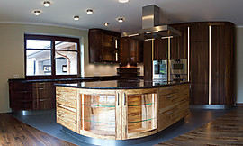 Dunkles Nussbaumholz und das helle Holz der Trüffelbuche wurden bei dieser runden Küche kombiniert. Geschwungene Glastüren, offene Regale und Beleuchtungseffekte lockern das Gesamtbild auf. Zuordnung: Stil Design-Küchen, Planungsart Detail Küchenplanung