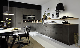 Für einen modernen Look der l-förmigen Küche sorgen Küchenfronten in naturgetreuer Betonnachbildung. Die Arbeitsplatte und Regale sind in heller Holz-Optik gestaltet und setzen einen schönen Farbkontrast. Zuordnung: Stil Design-Küchen, Planungsart Küche mit Sitzgelegenheit