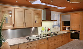 Dezente Rahmenfronten, helles Massivholz, Oberschränke mit Glasfront und eine hellgraue Granitarbeitsplatte vereinen sich hier zu einer attraktiven Küchenplanung. Zuordnung: Stil Landhausküchen, Planungsart U-Form-Küche