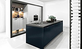 Wie Tag und Nacht und doch voll Harmonie: die Kücheninsel in Midnight Blue steht in attraktivem Kontrast zu den hellen Fronten in Daylight Grey. In dieser Designküche verschmelzen klassische Schönheit und Modernität zu einem harmonischen Ganzen. Die Küchenfronten mit Rillen-Struktur wirken sehr behaglich, weshalb sie auch beispielsweise bei Landhausküchen sehr beliebt sind. Zuordnung: Stil Design-Küchen, Planungsart Küche mit Küchen-Insel