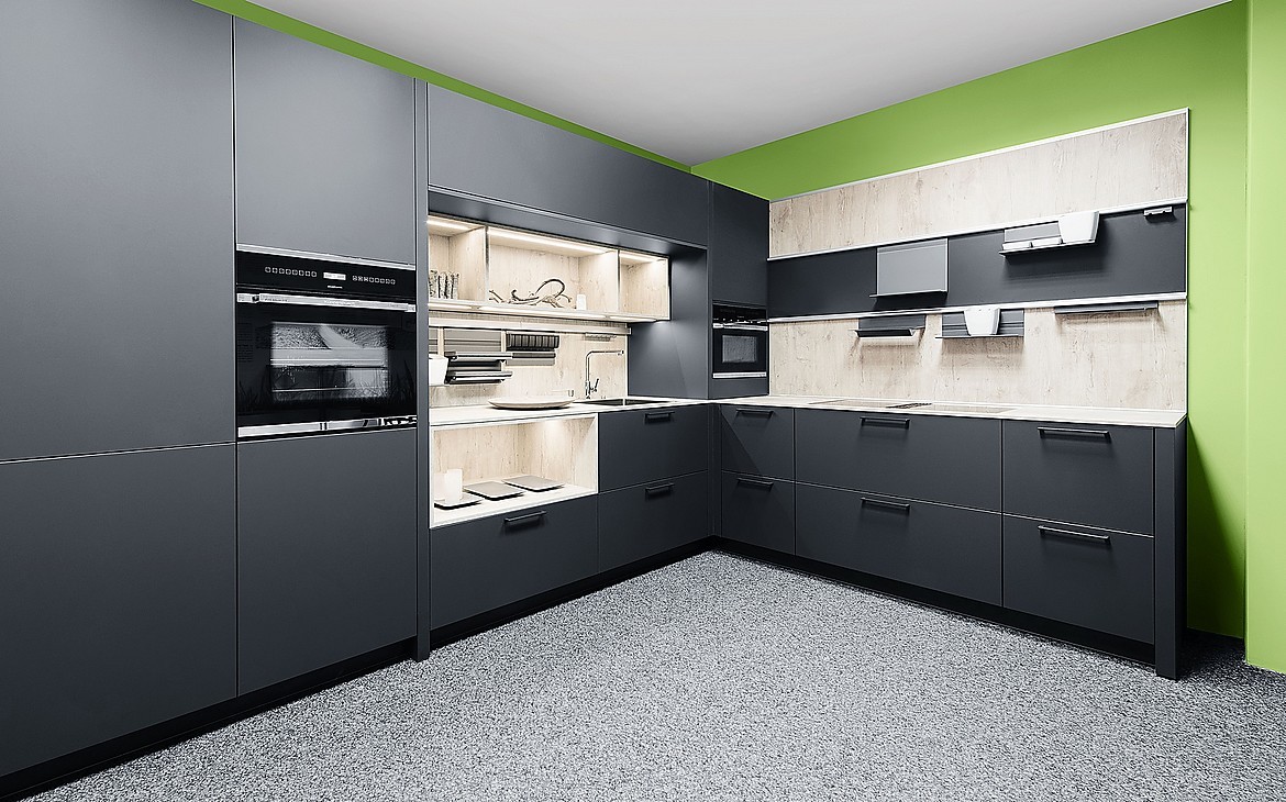 Diese L-Küche wirkt aufgrund der carbon-schwarzen Front sehr edel. Zur Gestaltung der Küchenrückwand und der Arbeitsplatte wurde ein helles Holzdekor genutzt, das alle Blicke auf sich zieht. Zuordnung: Stil Moderne Küchen, Planungsart L-Form-Küche