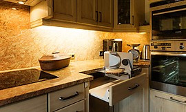 Diese ländliche Küche aus Tannenholz besticht mit praktischer Innenausstattung wie der in der Schublade verbauten Brotschneidemaschine. Zuordnung: Stil Landhausküchen, Planungsart Küche mit Küchen-Insel