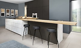 In dieser Designerküche treffen klare Linien auf weiße Natursteinoptik und dunkles, warmes Braun. Verbunden werden die Elemente durch eine Holztheke. Zuordnung: Stil Landhausküchen, Planungsart Küche mit Sitzgelegenheit